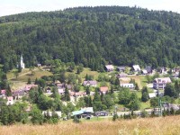 Střed obce v létě: Z lesa nad obcí nenápadně vyčnívá rozhledna Královka.