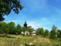 spätný pohľad na kostolík zasadený medzi stromami na vrcholku nad dedinou