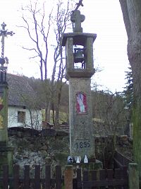 Kamenná zvonička z roku 1895 v Myslkově (Miskově). V pozadí křížek na kamenném podstavci.