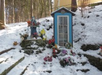 Dřevěná minikaplička a socha Panny Marie Sedmibolestné v obležení umělých květin