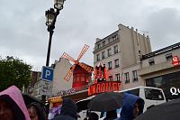 pohľad na Moulin Rouge a na tváre schovávajúce sa pred dažďom
