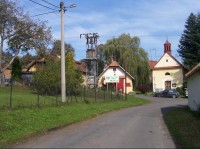 Jílovec: Pohled na náves v obci s uvítací cedulí a kaplí