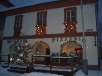 Zasněžený vánoční stromek před muzeem s pizzerií
