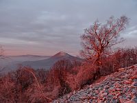 Paprsky vycházejícího slunka ozařují rudě Milešovku a jižní svah- suťové pole hory Kletečná.