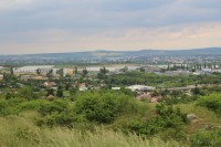Pohled z vrcholu na průmyslový areál v městské části Slatina, za ním předměstské čtvrti na jihu Brna, na horizontu zalesněný hřeben Ořechovské pahorkatiny s dominantním Nebovidem