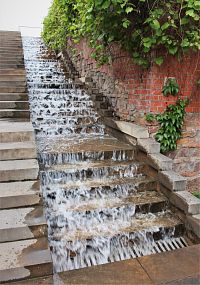 Voda kaskádovitě klesá po betonových schodech vedle schodiště
