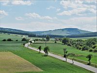 Pohled podél hlavní komunikace k obci Vrbovce, na horizontu výrazný kopec Bojiště