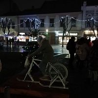 biely bicykel, po roztočení pedálov sa rozsvieti neďaleký vianočný stromček