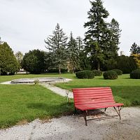 červená lavička v parku a bývalý bazén s vodometom