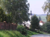 Hodslavice: Pohled na cestu od Mořkova, vlevo hřbitovní zeď, v pozadí jeden ze tří místních kostelů