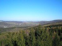 od stožárů: vesnice Deutschneudorf (vlevo hluboko v údolí) a Nová Ves v horách (šplhající do svahu), na obzoru panorama Českého středohoří